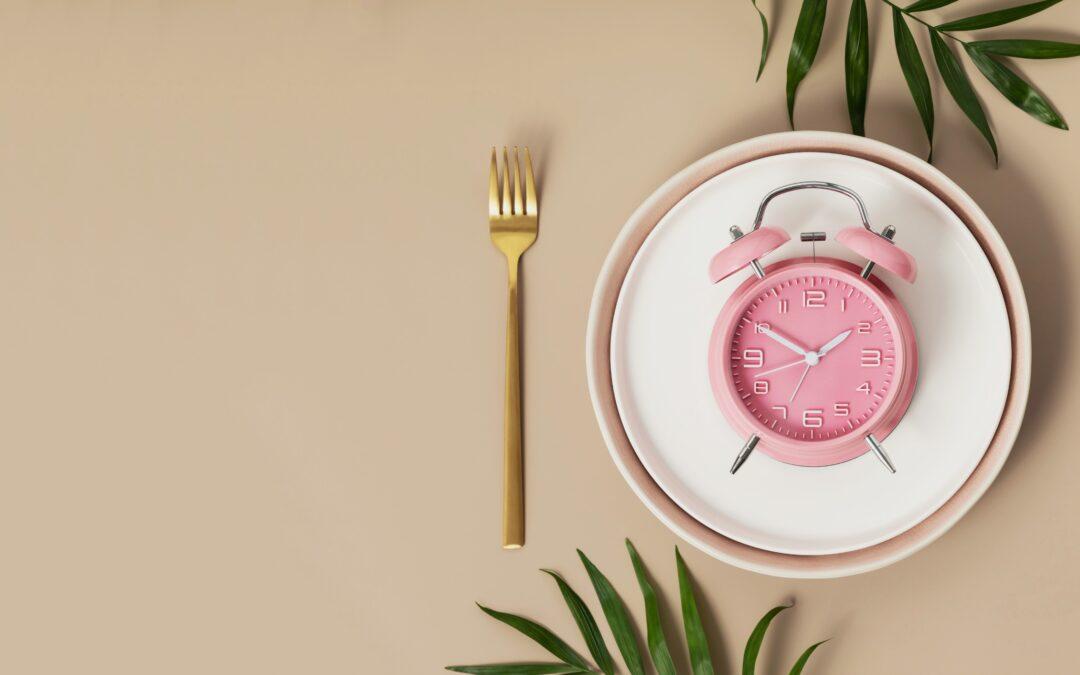 Alarm clock on a plate with cutlery, symbolizing time-restricted eating and intermittent fasting schedule.