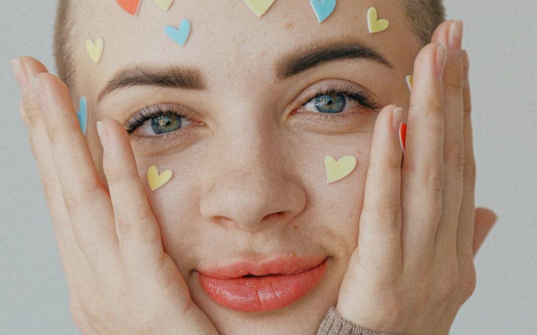 Close-up of a smiling person with colorful heart stickers on their face, representing self-love and positivity.