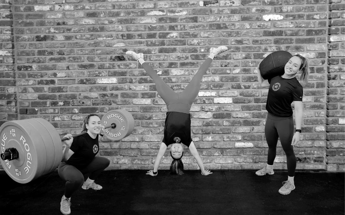 Kira Vargas demonstrating strength and fitness skills in a gym, performing a handstand, with a barbell squat and a medicine ball hold in the same frame.